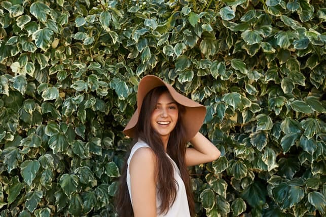 a woman is a big hat is smiling and posing outdoors