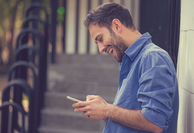 a happy man in a blue shirt is checking his phone