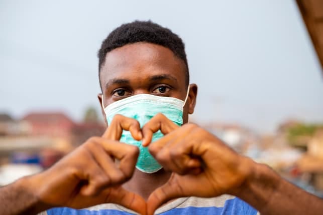 a young african man wearing a facemask and making a heart sign