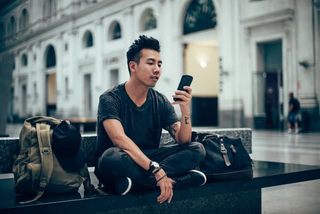 a modern asian guy checking his phone outdoors