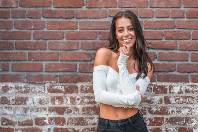 a woman is a white sweater posing with a brick wall