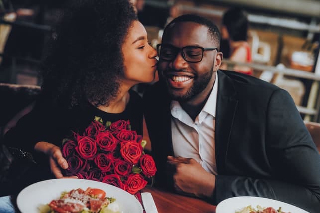 a woman kissing her boyfriend on a date while holding flowers
