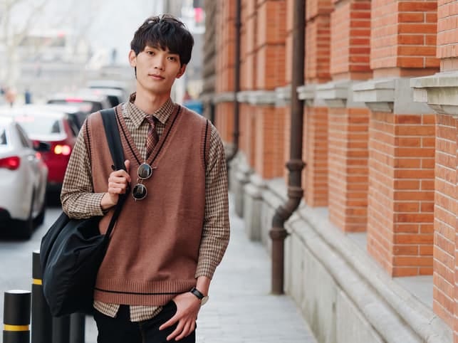 a young Asian man in a fashionable sweater is posing outside