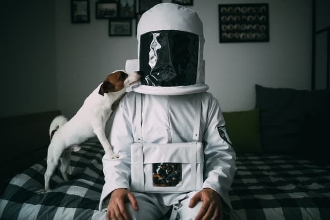 a man in a spacesuit sitting on his bed with his dog
