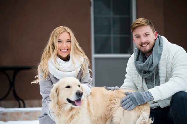 an attractive blonde couple with a dog outdoors in winter