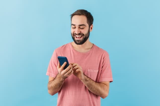 a happy guy in a pink shirt is checking his smartphone