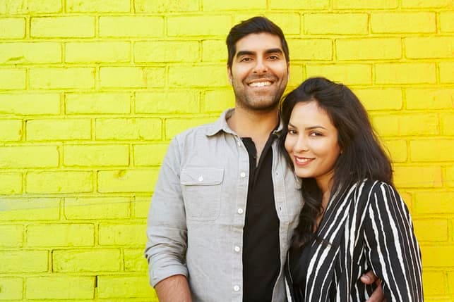 an adult oriental couple is posing and smiling together on a yellow background